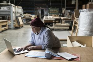 a black female carpenter working on a lap top computer after work hours in a large woodworking